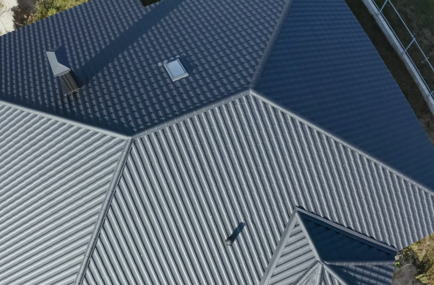 Aerial view of a house roof with dark blue shingles and a light gray metal section.
