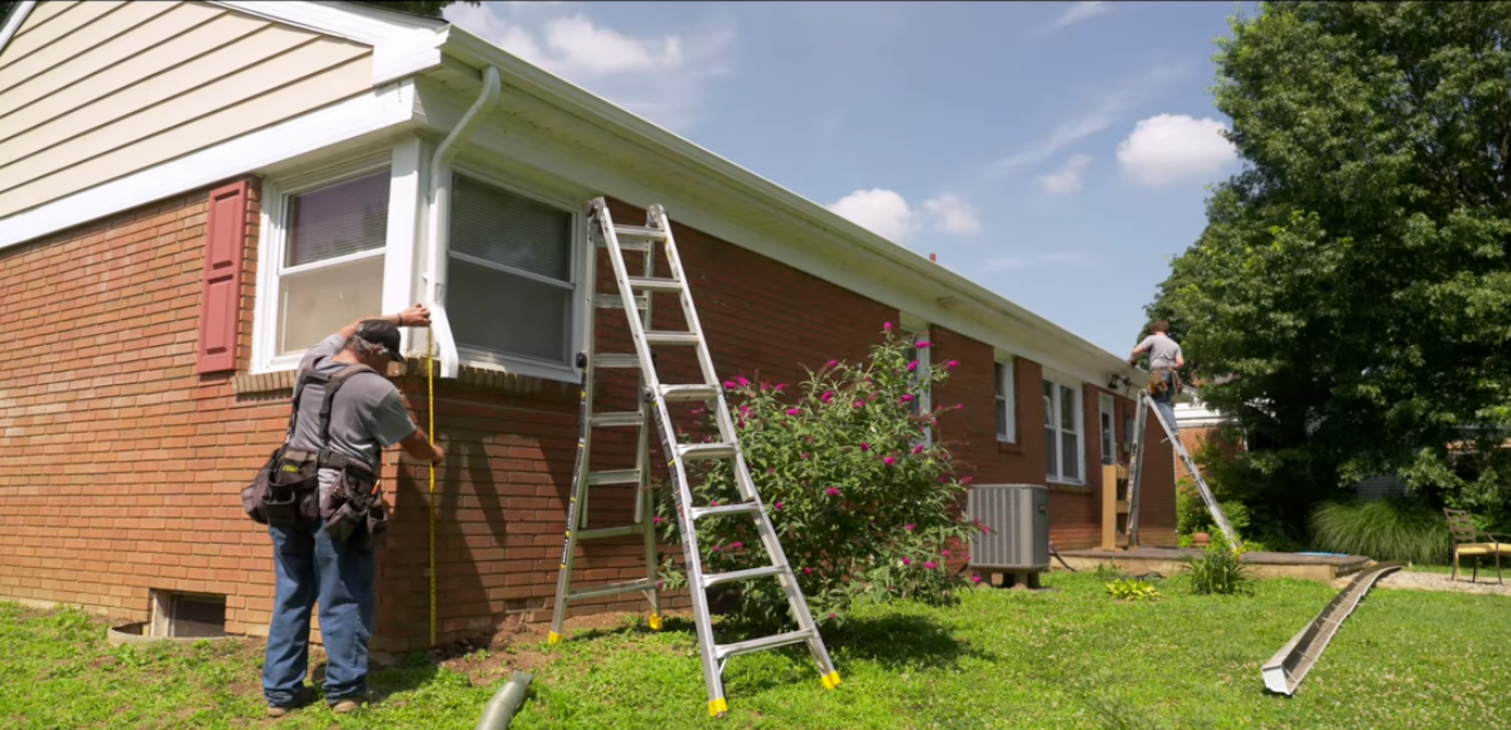 Workers painting a brick house exterior from ladders on a sunny day