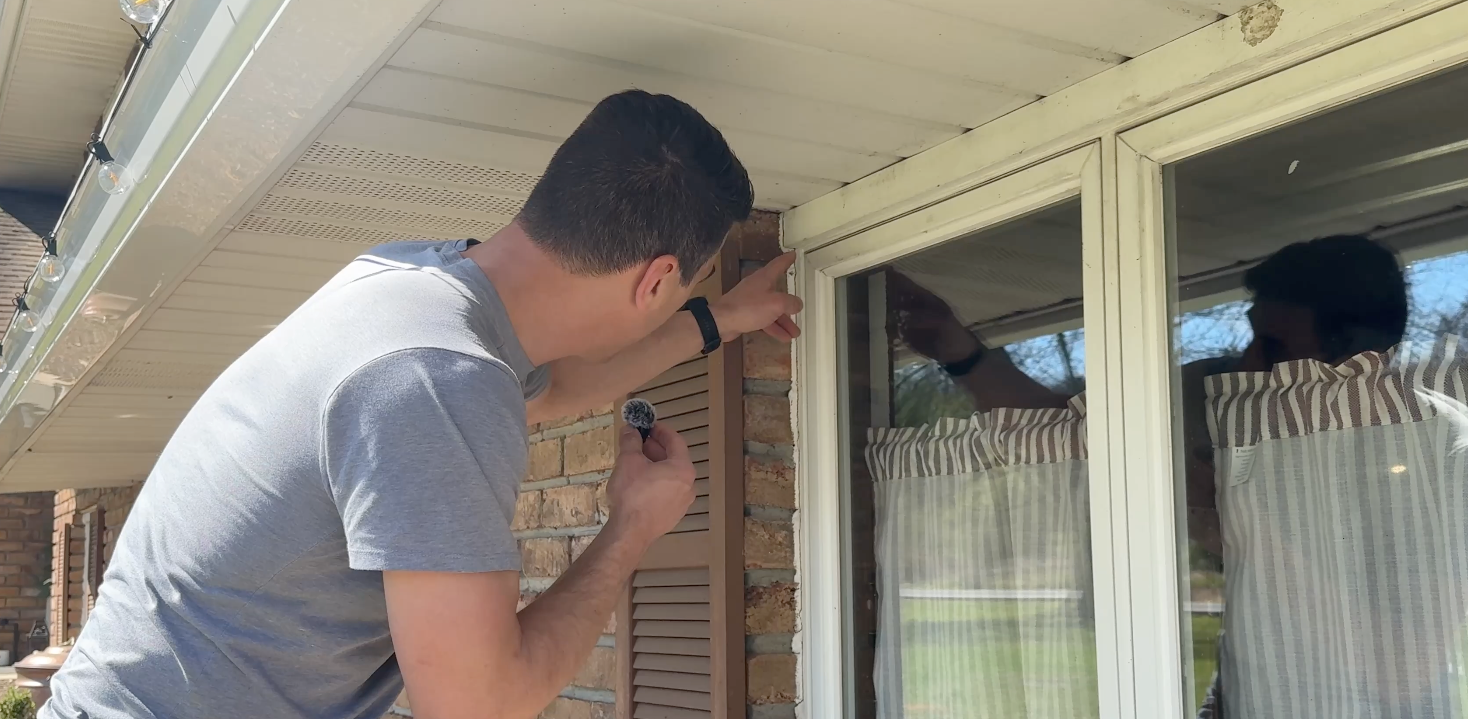 Man installing trim around a window on a house exterior with a screwdriver
