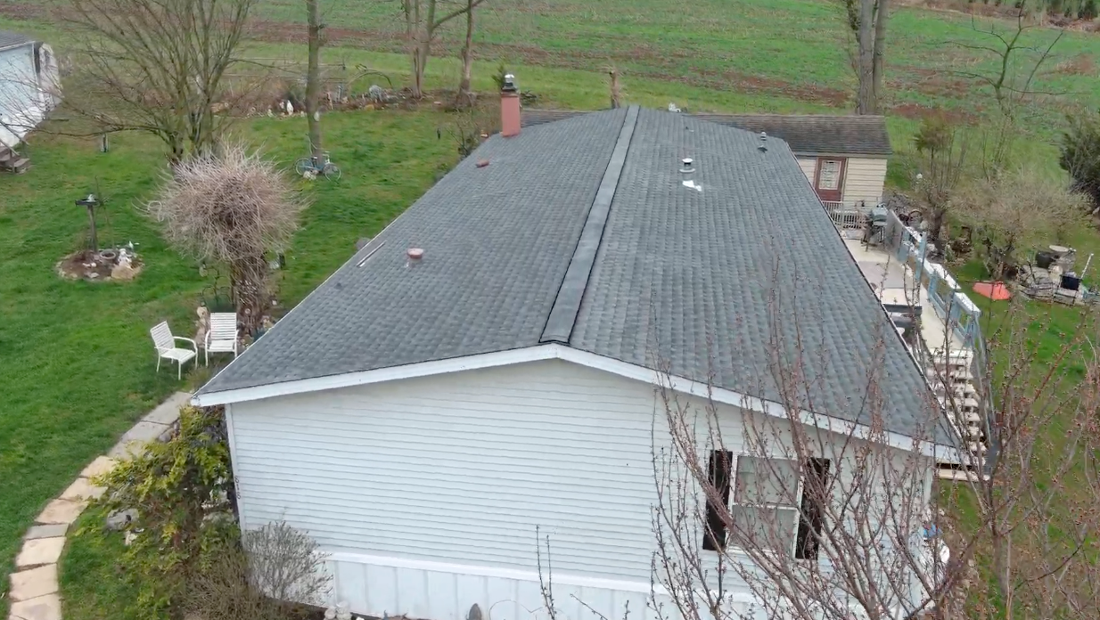 Aerial view of a white house with a gray roof surrounded by grass and bare trees
