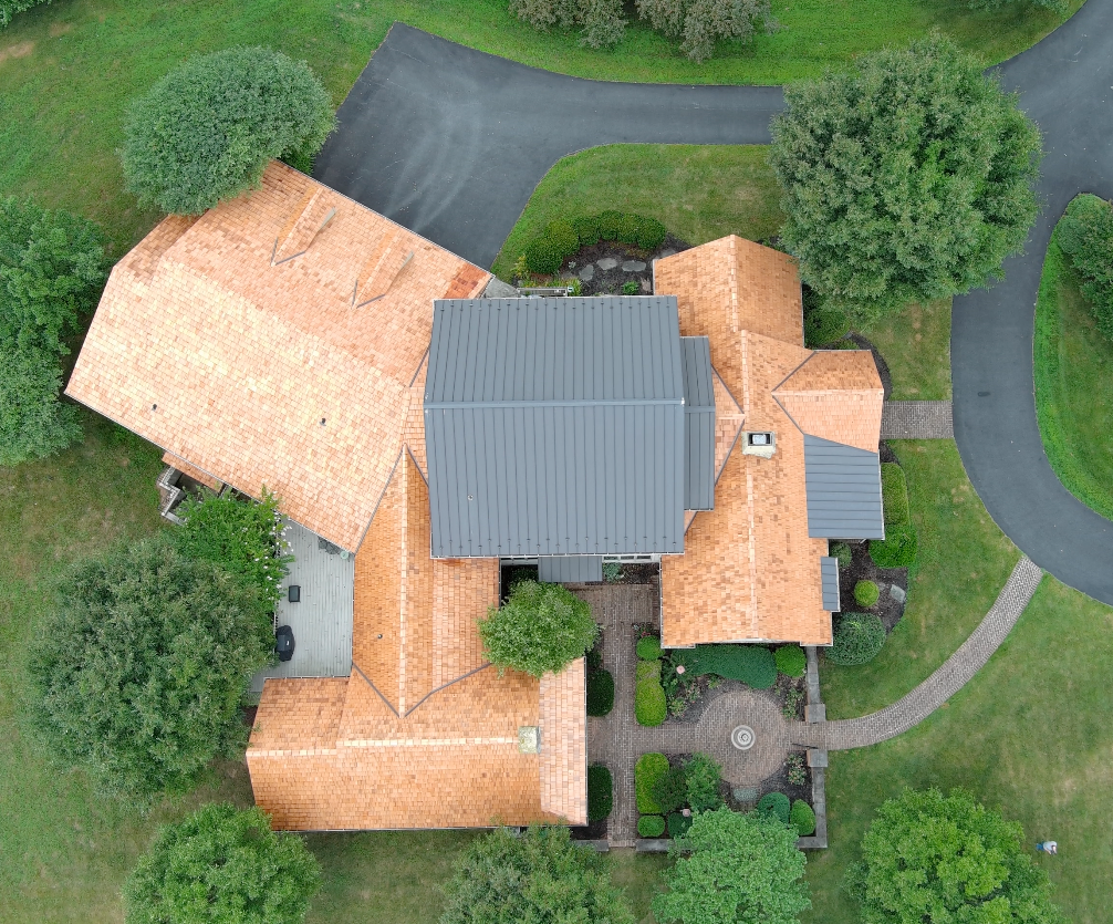 Aerial view of a house with orange roof and gray center roof, surrounded by trees and curved driveway