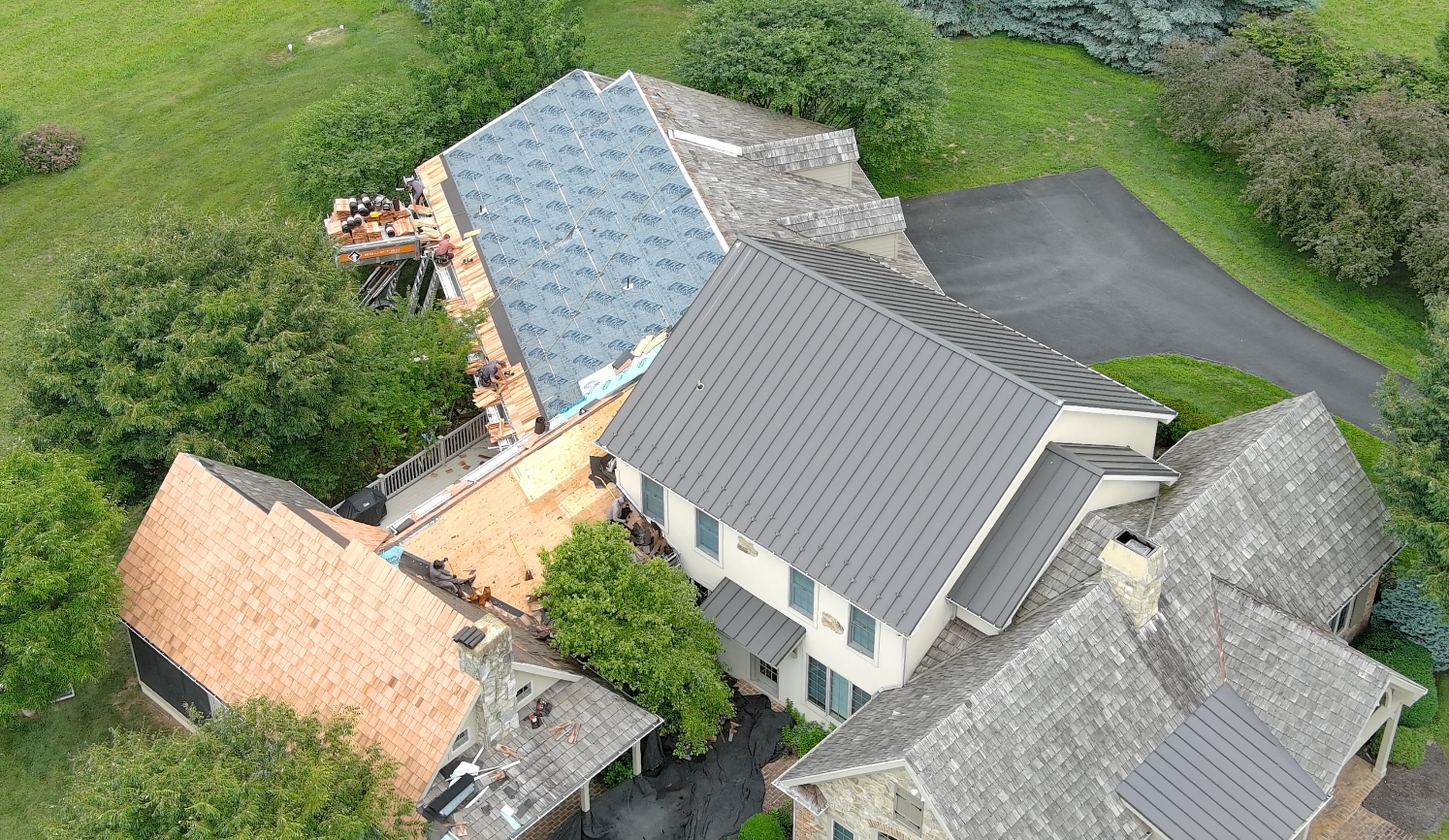 Aerial view of several houses with gray roofs beside a green yard and driveway.