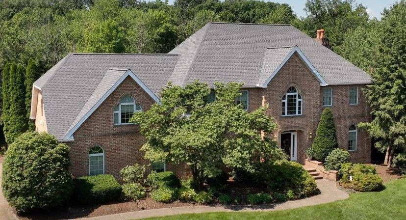 Two-story brick house with a gray roof and lush green landscaping.