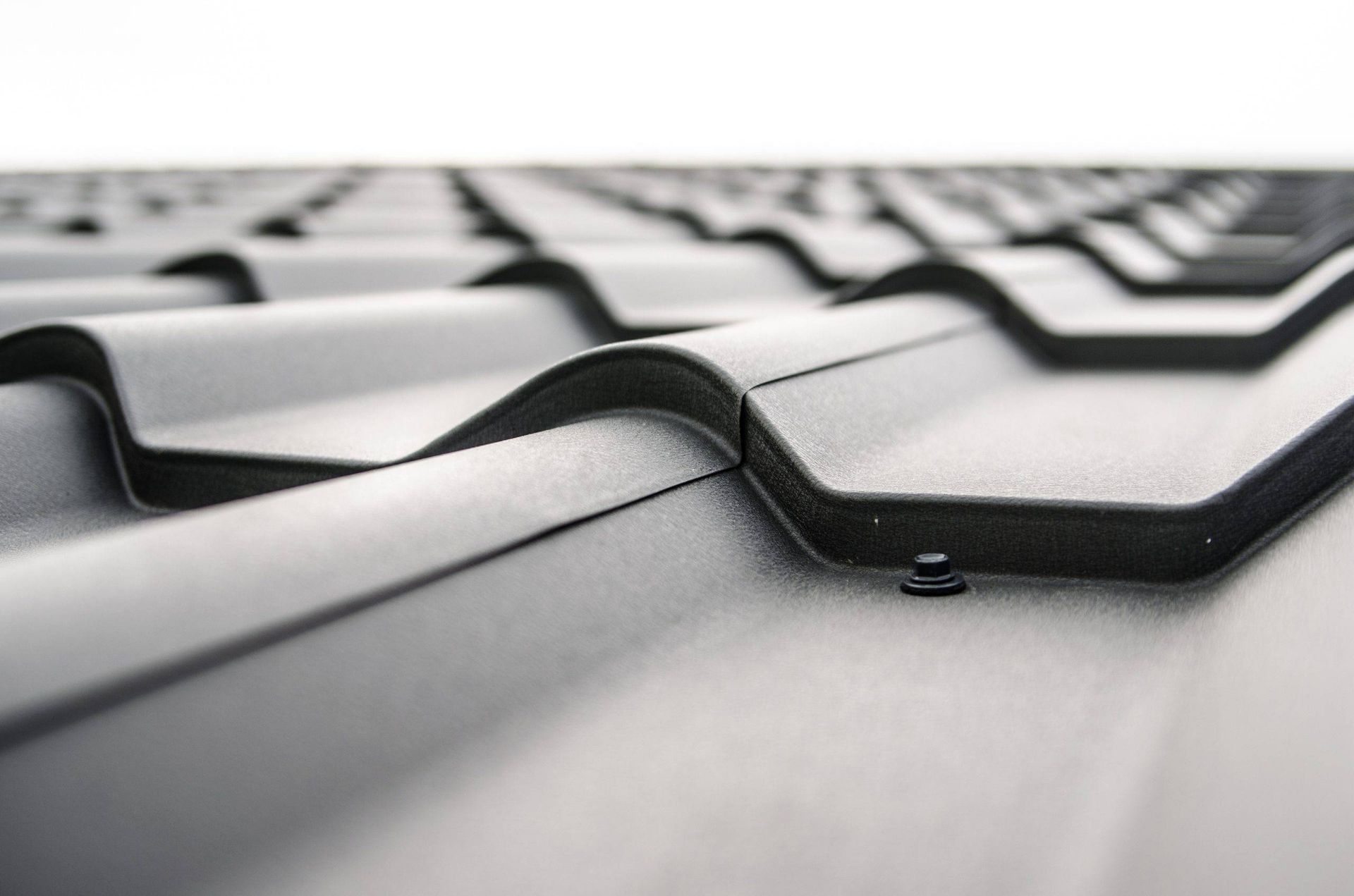 Black metal roof tiles, textured with curved ridges, close-up shot.