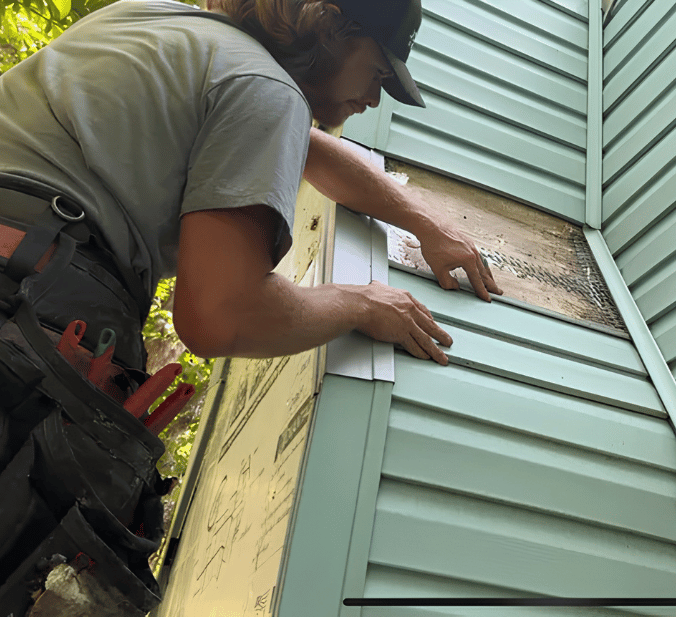 Man in hat installing siding on a corner of a house.