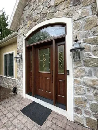 A dark wood front door with sidelights and arched transom, set in a stone facade. Two lantern lights flank the door.