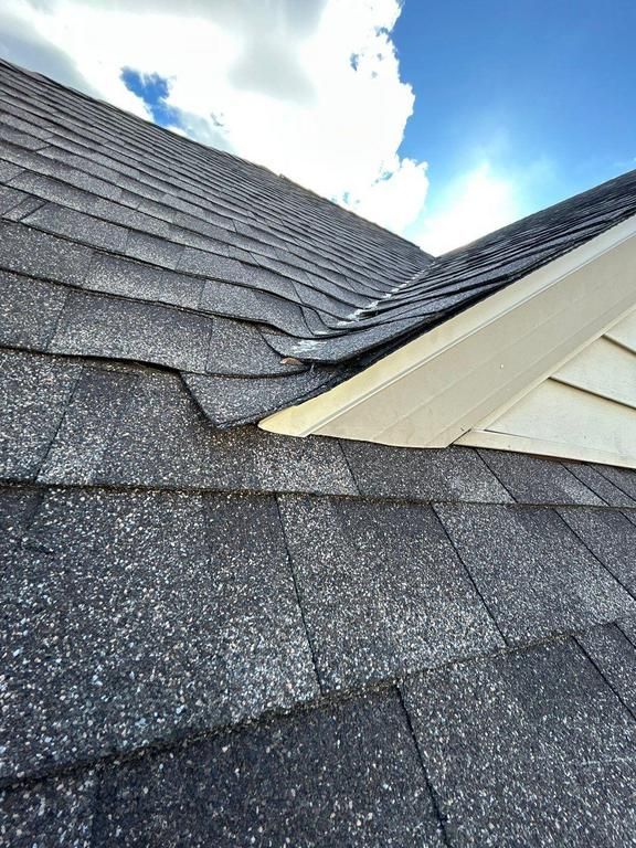 Damaged roof shingles and bent white gutter at a roof valley under a blue sky