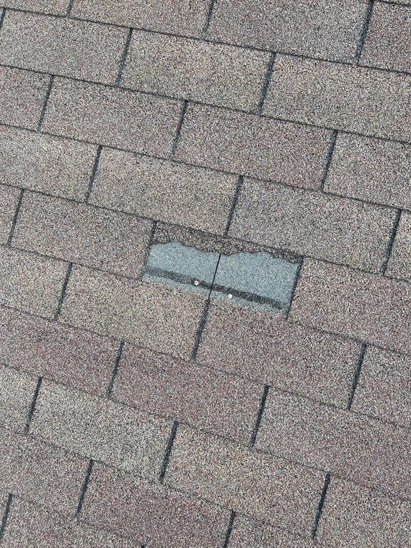 Close-up of gray asphalt shingles with a small broken patch exposing the underlayment.
