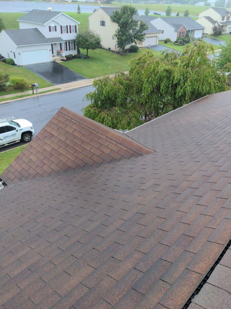 View from a rooftop over a suburban neighborhood with wet shingles and parked cars after rain