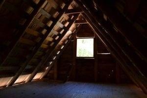 Wooden attic interior with a central window and rafters.