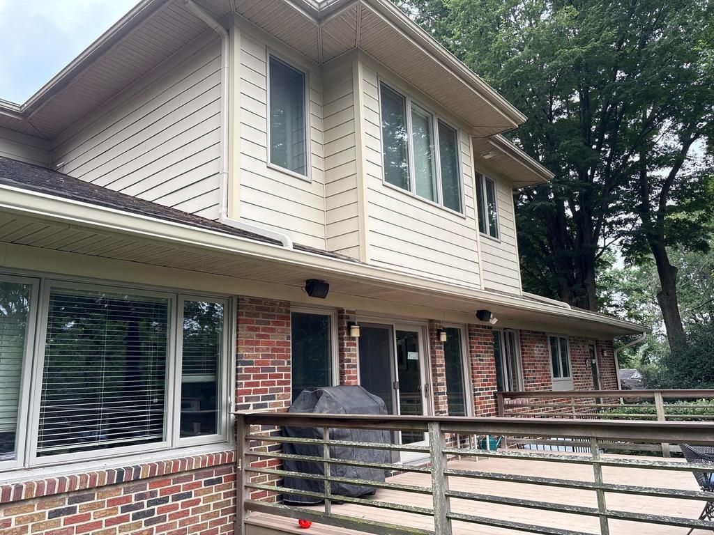 Split-level house with gray siding, brick, and a small porch; green lawn, trees, and an American flag.