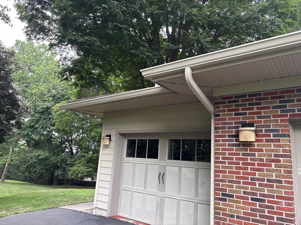 A light-colored garage with a windowed door and an attached brick wall, set under a mature tree.