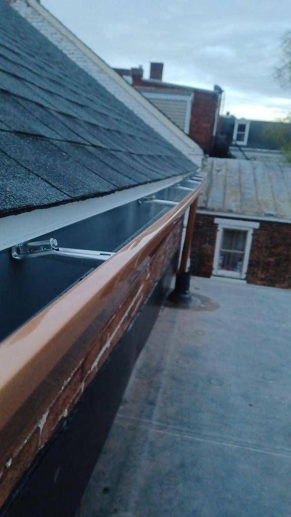 Black shingle roof with copper gutters on a brick building, overcast sky in background.