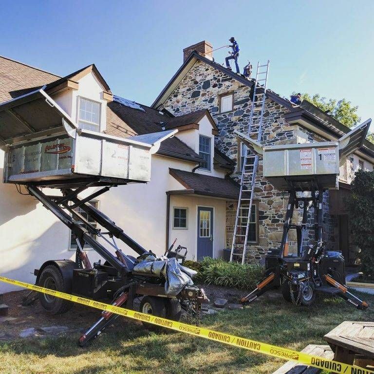Two roofers on a roof, working with lift equipment, yellow caution tape on the grass.