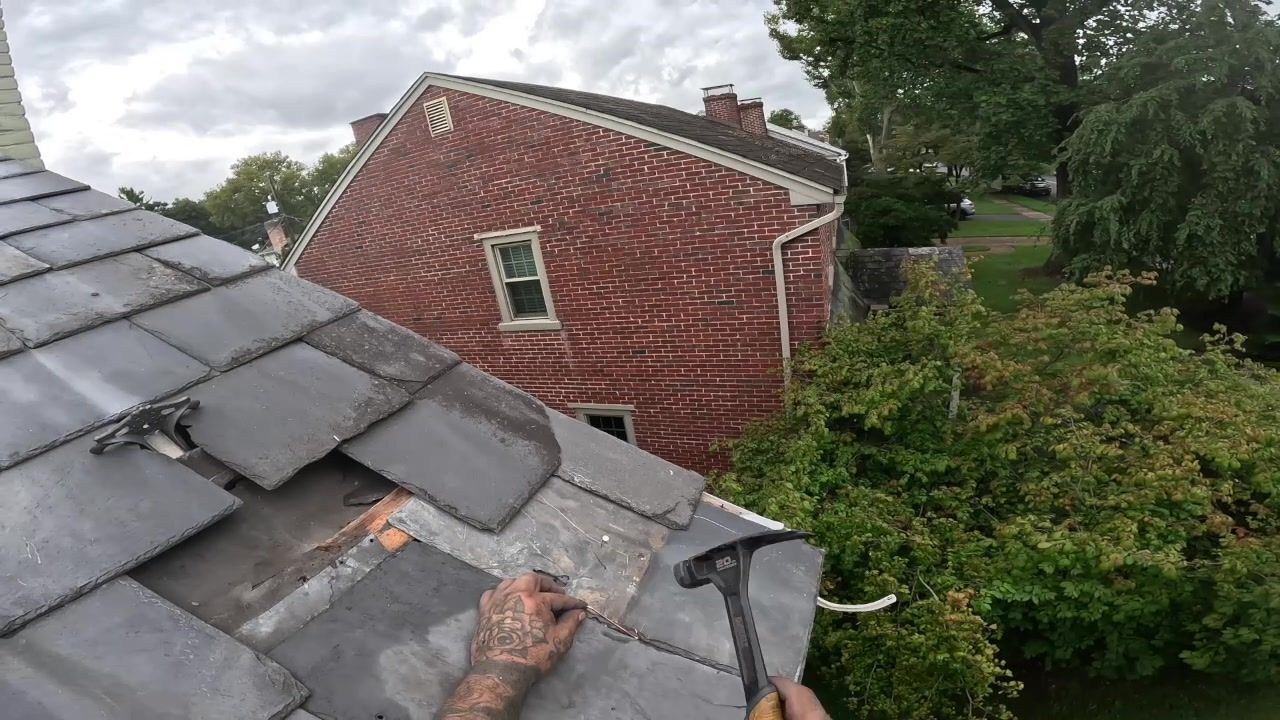Roofer installing a slate hook before sliding replacement slate into position