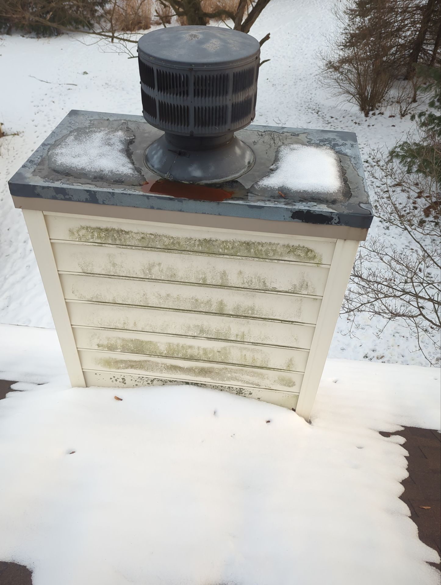 Metal chimney chase cover with visible rust, deteriorated sealant, and snow accumulation on a residential roof in Quarryville, PA.