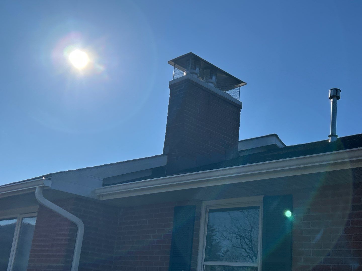 Bright sun over a brick house roof with a tall chimney and blue sky