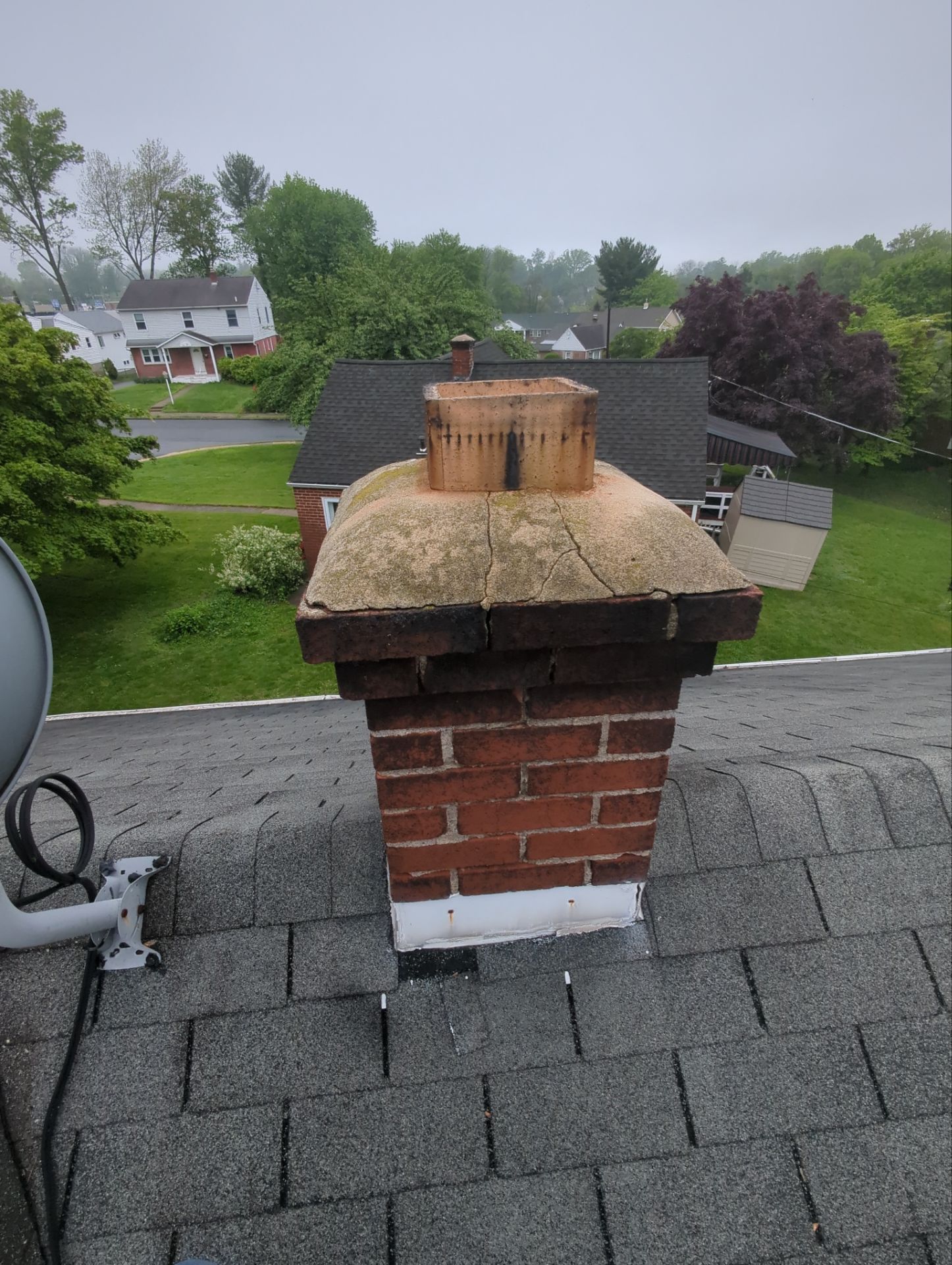 Brick chimney with weathered crown and asphalt shingles on Hillside Road