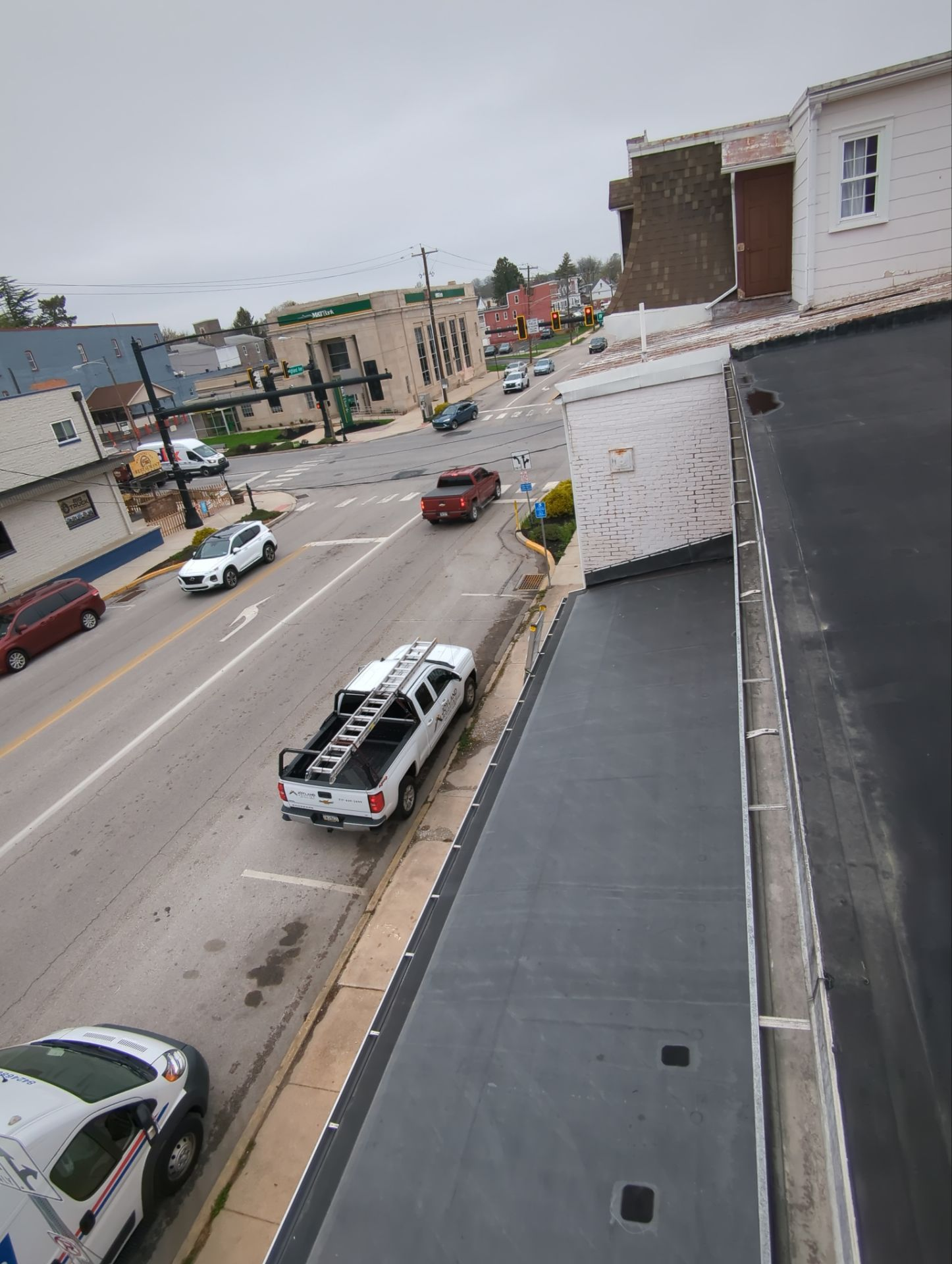 Street view from a rooftop with cars on a road beside buildings and parked vehicles.