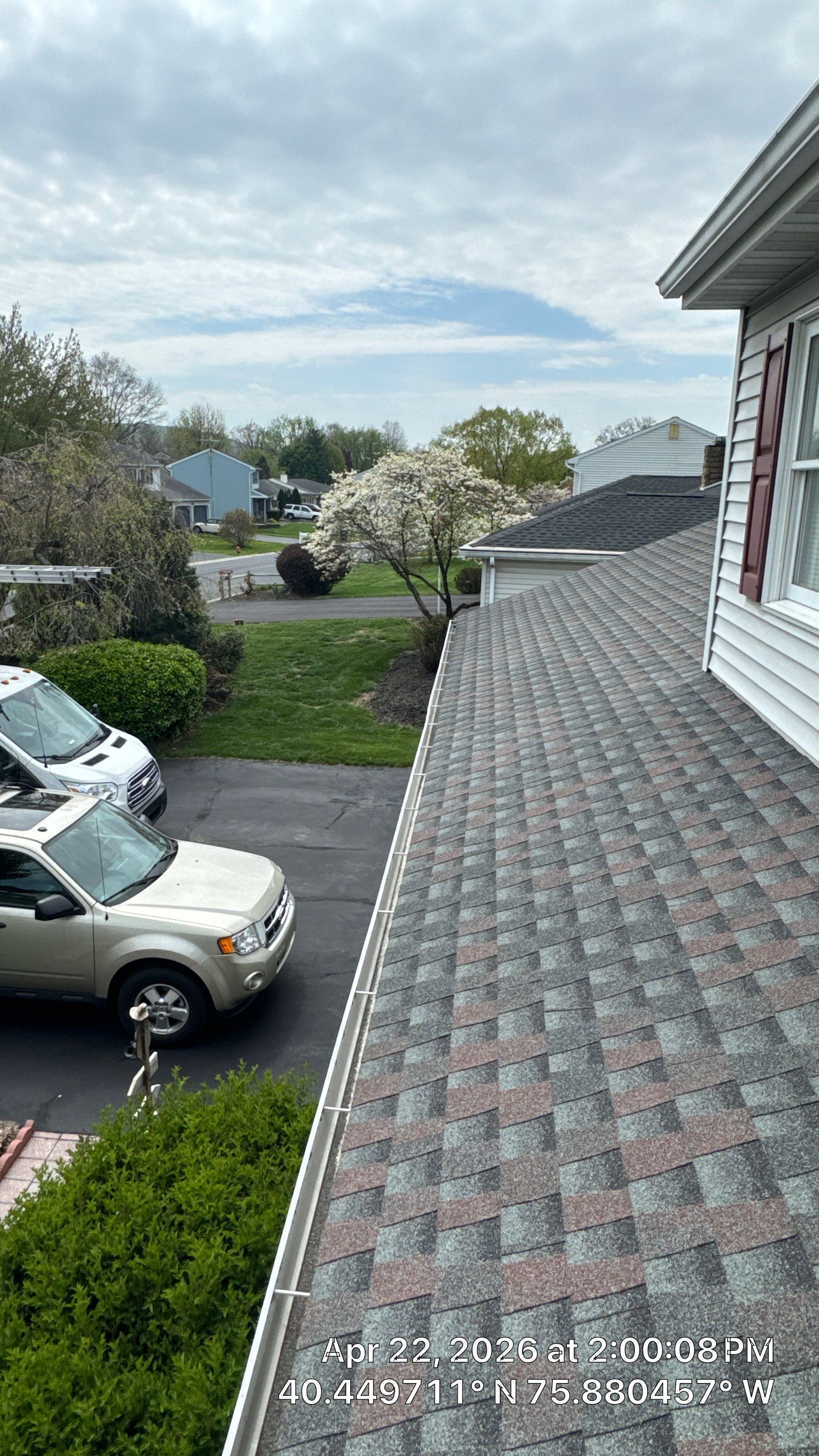 Suburban street view from a roof, with parked cars, trees, and a cloudy sky.