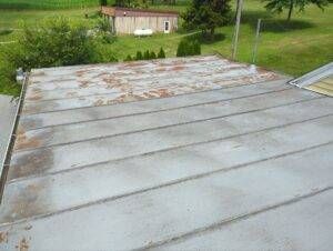 Weathered metal roof with rust-colored patches, in a grassy outdoor setting.