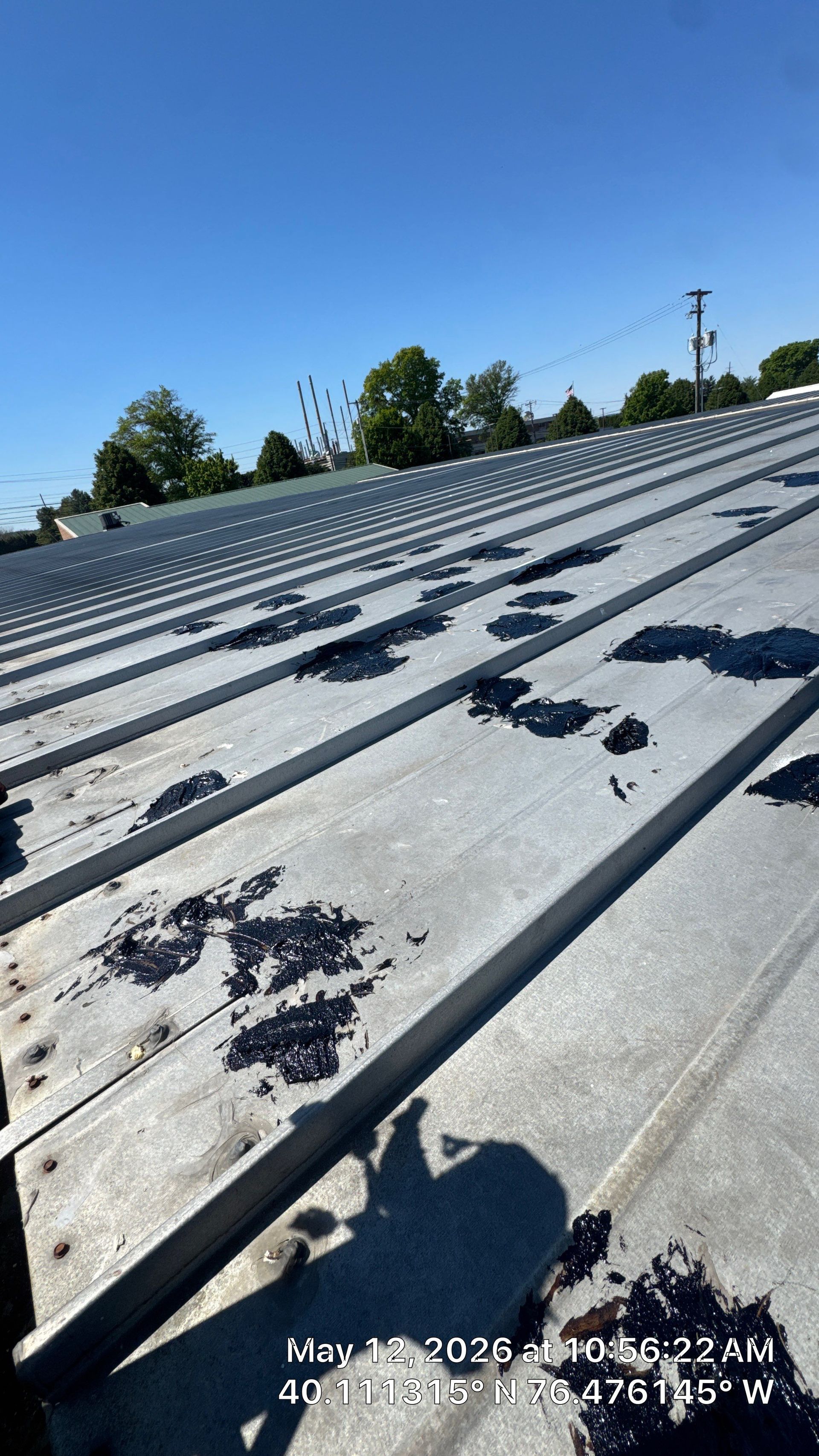 Sunlit corrugated metal roof with scattered dark debris under a blue sky