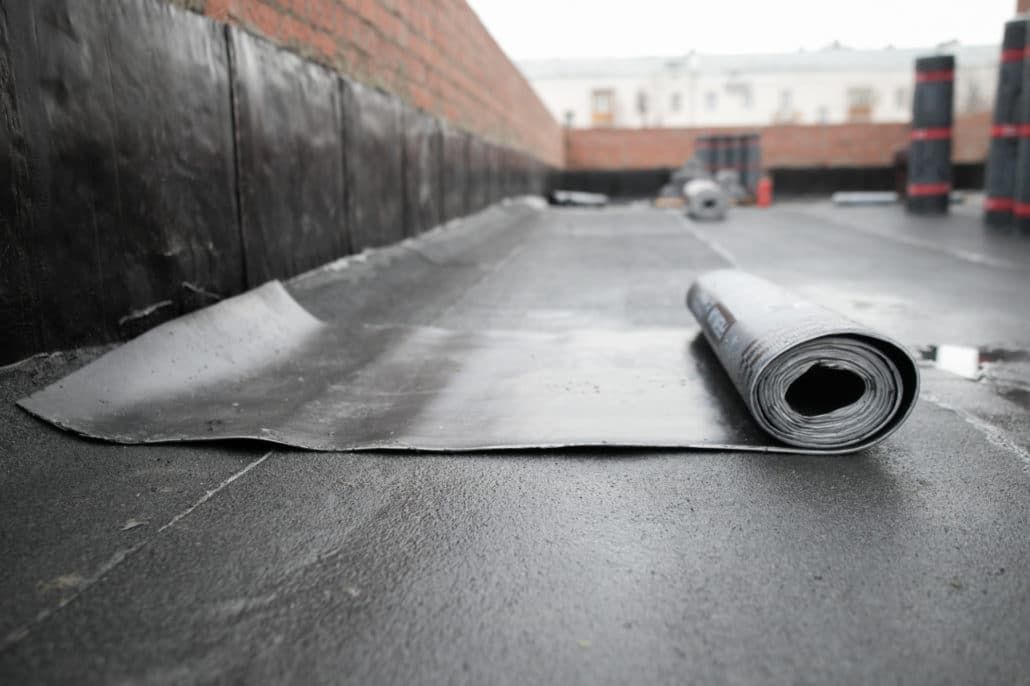 Rolled roofing membrane on a flat rooftop with one sheet laid out in the foreground