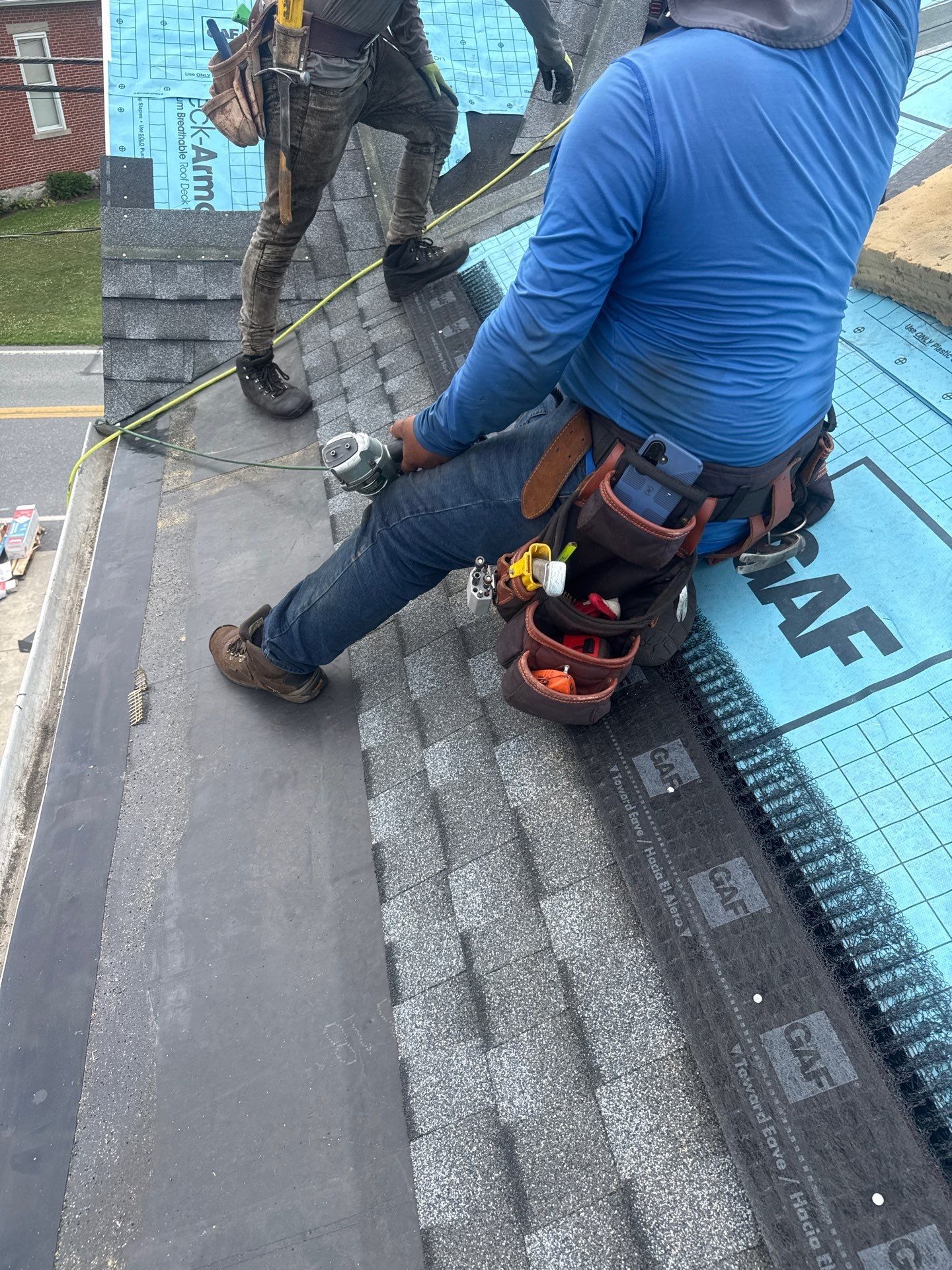 Roof workers installing underlayment on a sloped roof, with tools and materials nearby
