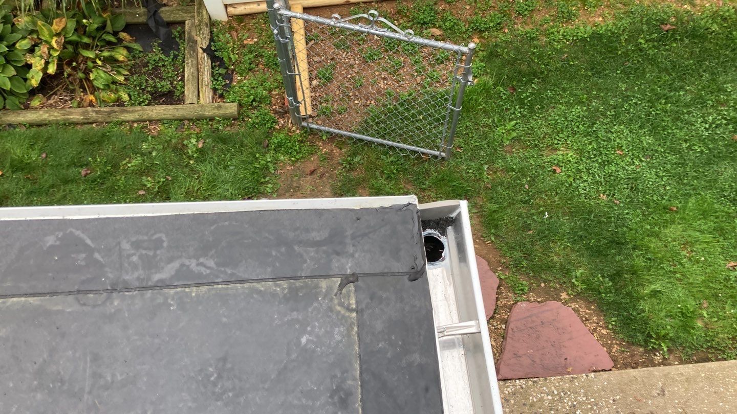 Roof edge beside a grassy yard and metal gate, with a concrete step below
