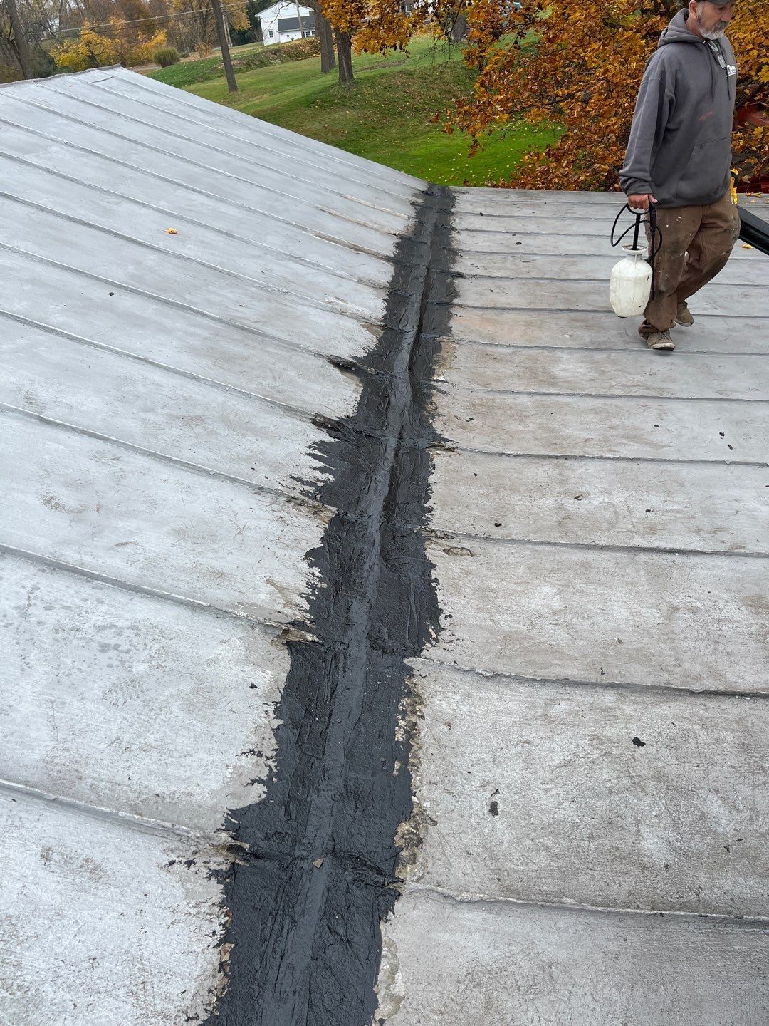 Roof seam being repaired with black sealant, with a worker standing beside it.