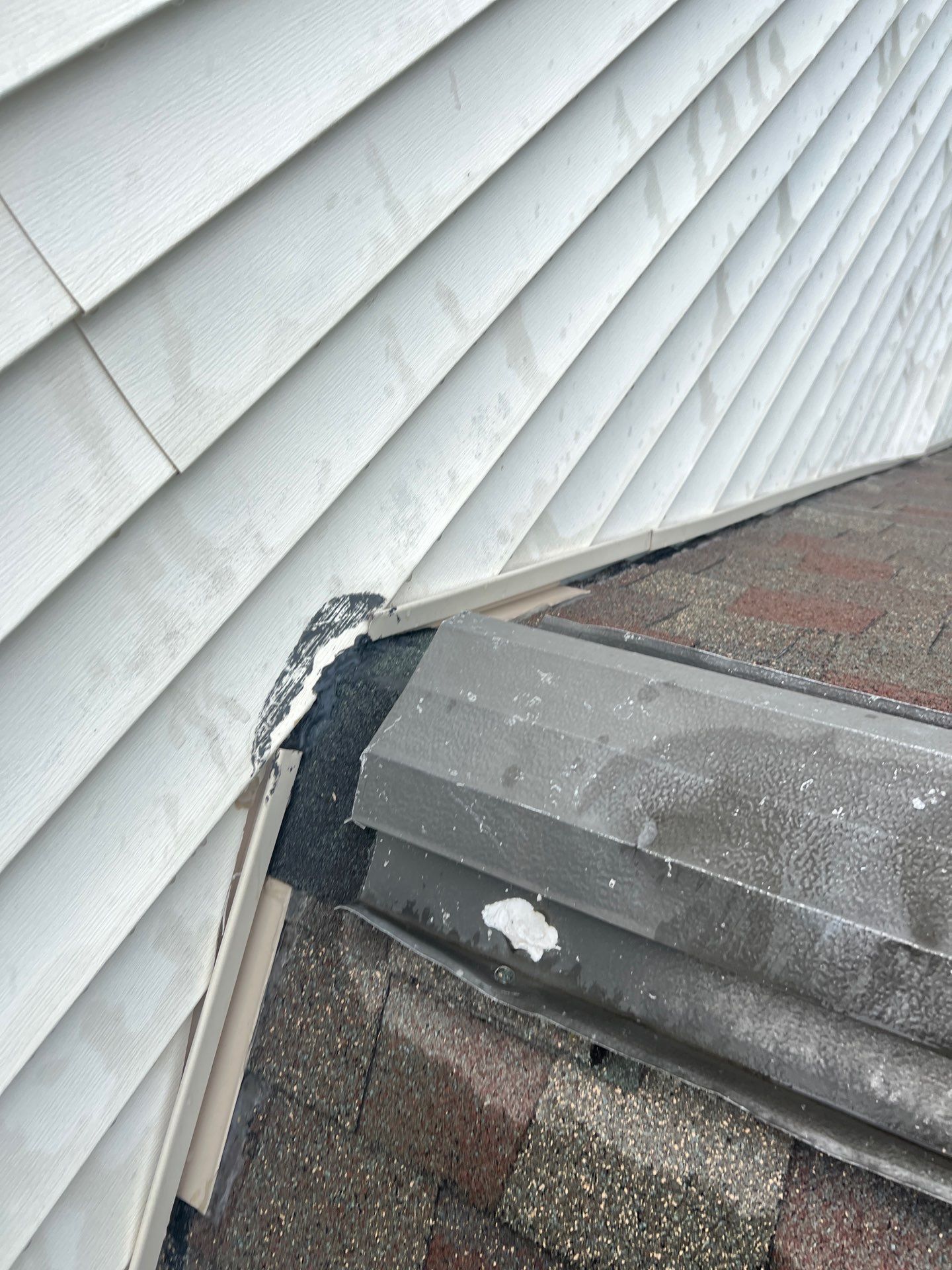 Damaged roof flashing where a shingled roof meets a white-sided wall
