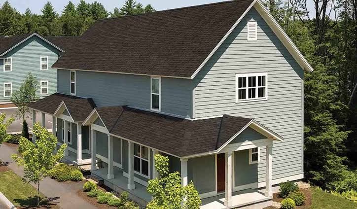 Two-story gray house with brown roof and front porch surrounded by trees
