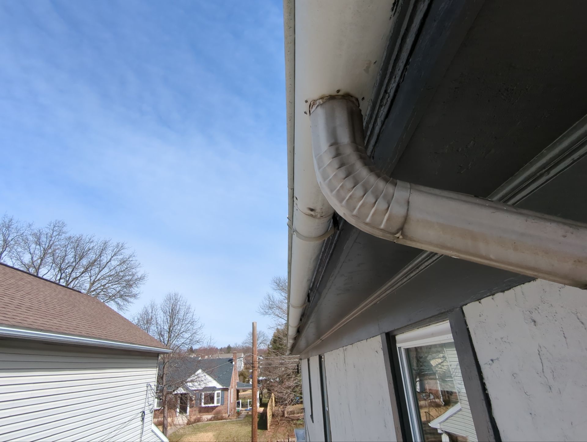 Aging white gutter and downspout system along a residential roof in Pottstown, PA