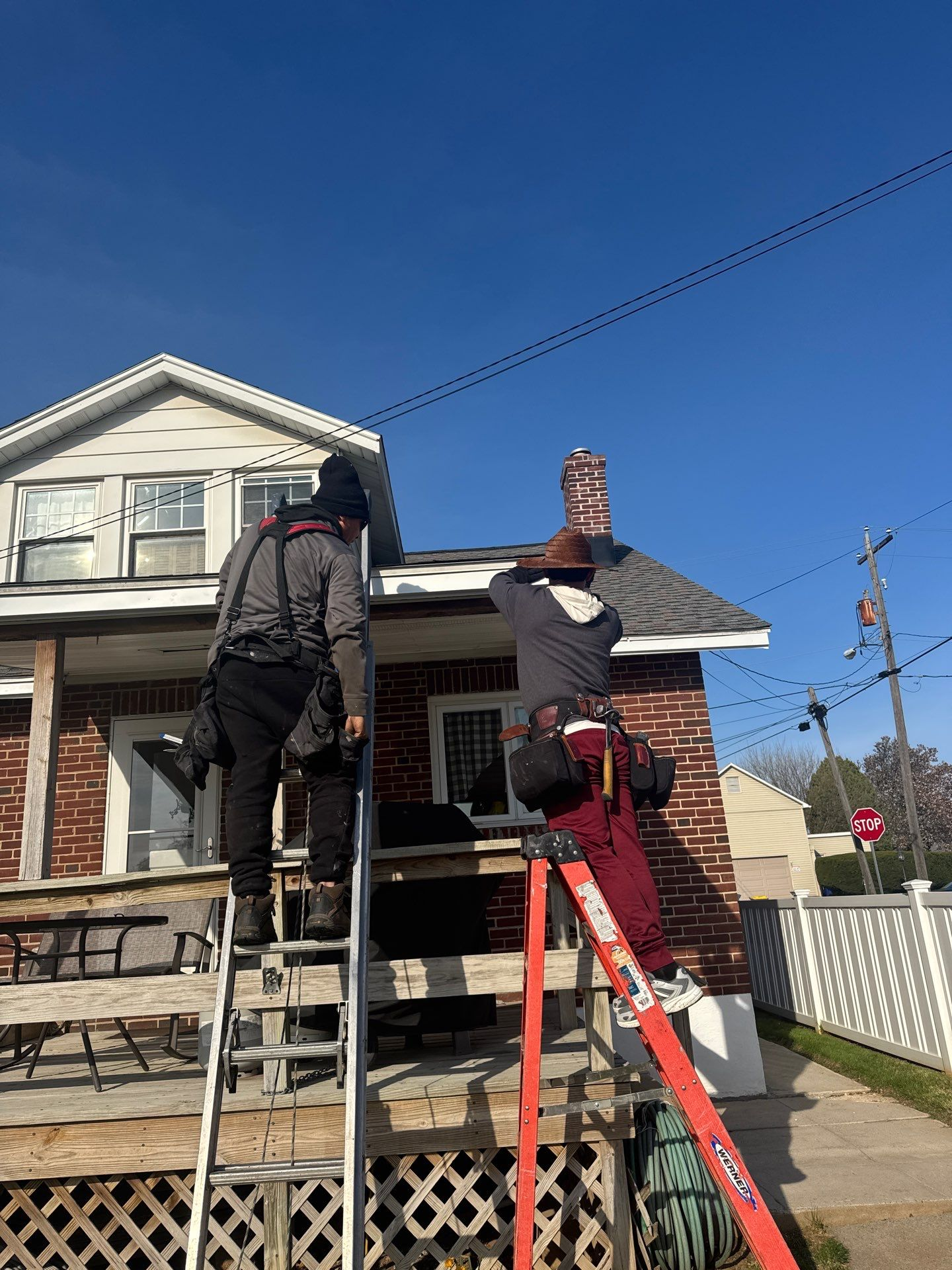 Two workers on ladders repairing the roof and brick chimney of a house on a sunny day