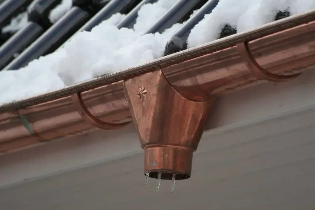 Copper gutter with snow on the roof, dripping water from the downspout in winter