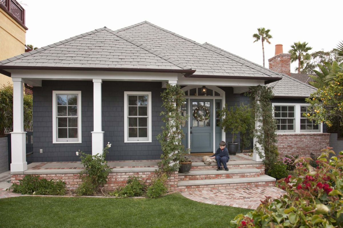 Dark gray craftsman-style house with white trim, front porch, garden, and stone walkway