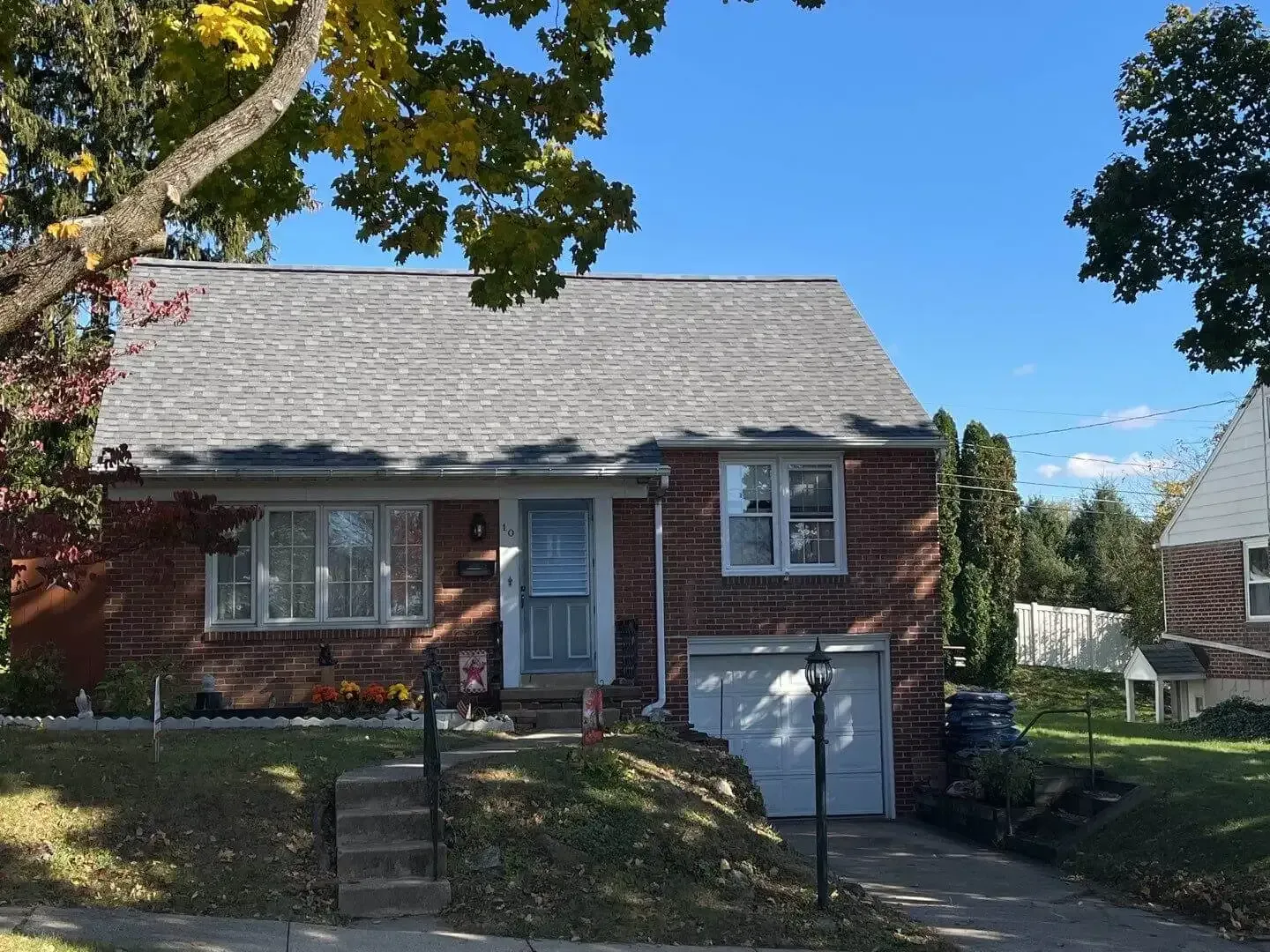 Brick house with white roof and front steps, partly shaded by trees on a sunny day.
