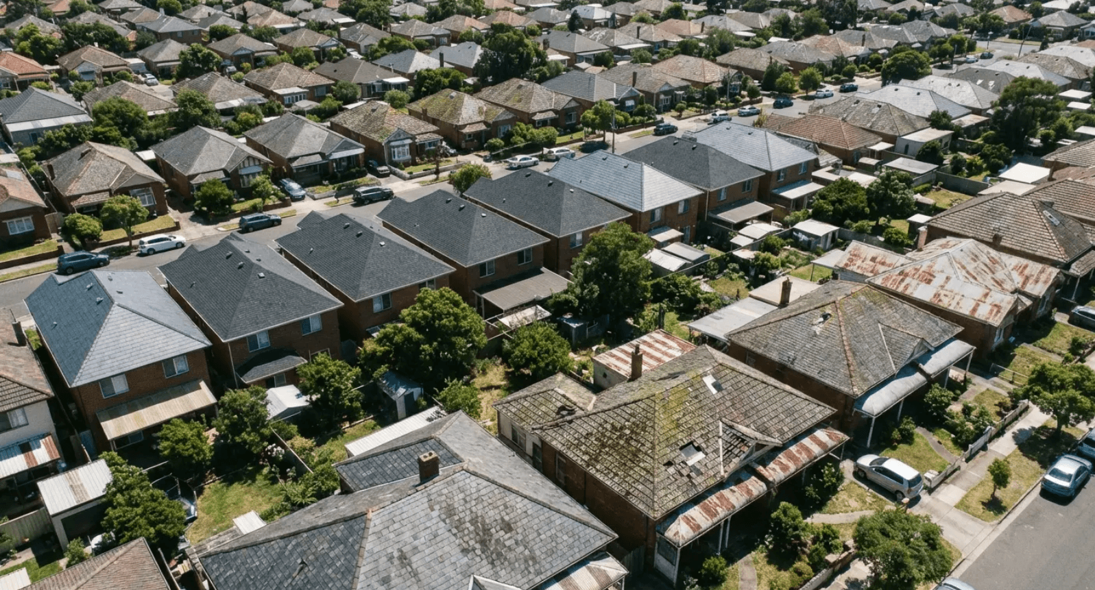 Aerial view of a dense neighborhood with rows of gray-roofed houses and tree-lined streets.