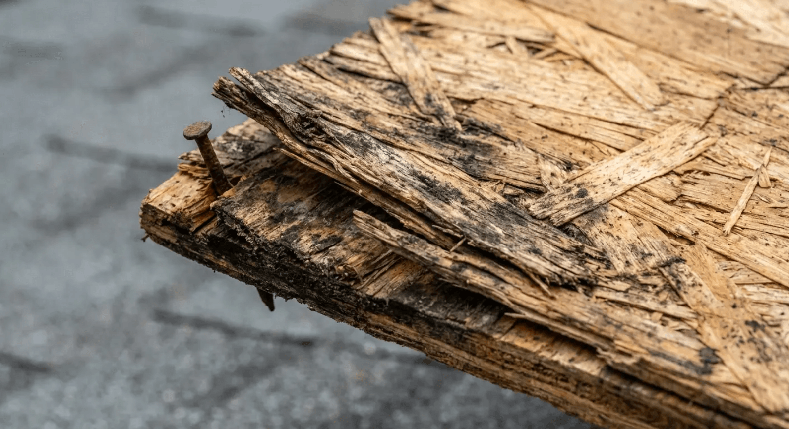 Close-up of a splintered wooden plank with rough, cracked edges on a gray surface