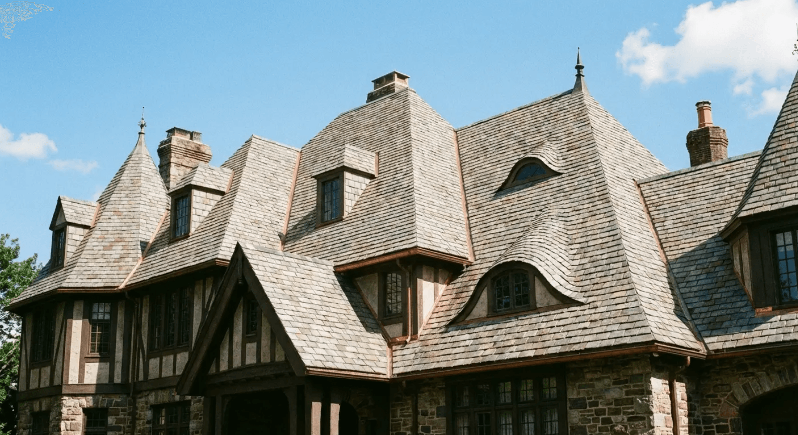 Historic stone-and-timber house with steep shingled roofs under a blue sky