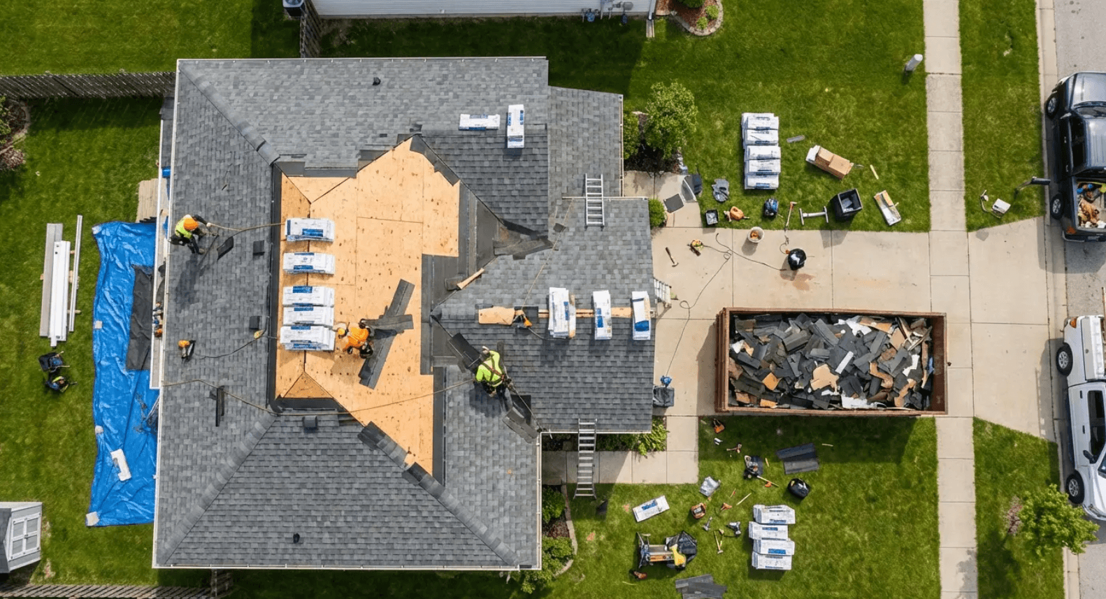 Aerial view of roofer crew replacing shingles on a residential home with debris dumpster nearby