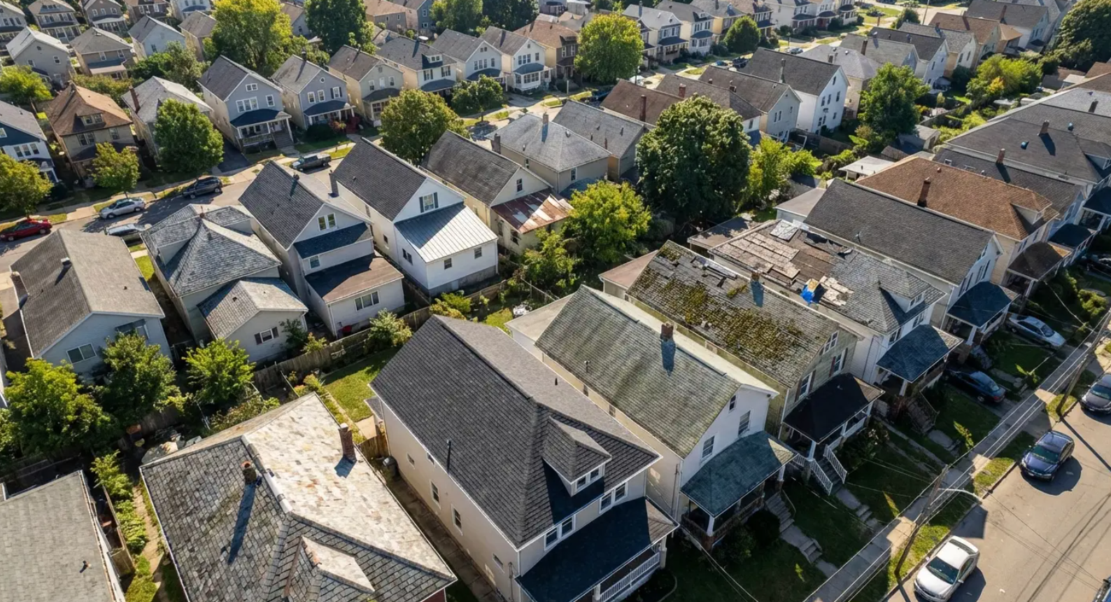 Aerial view of a suburban neighborhood with rows of houses and parked cars along a street.