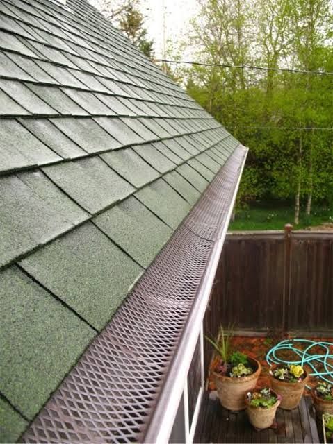 Rain-soaked green shingle roof with a metal gutter and a deck below, bordered by trees and a wooden fence