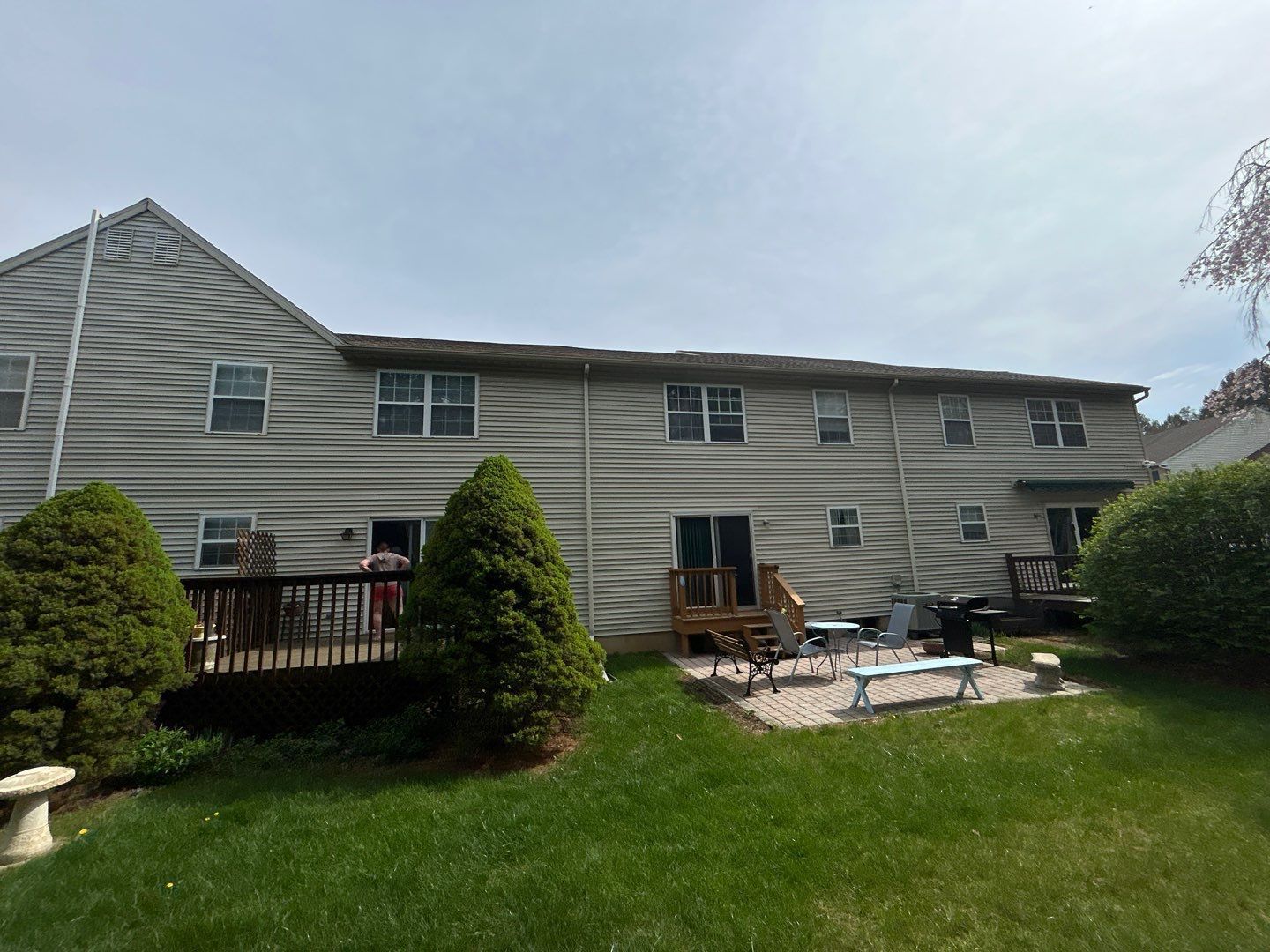 Backyard with two-story gray house, green lawn, deck, patio chairs, and shrubs