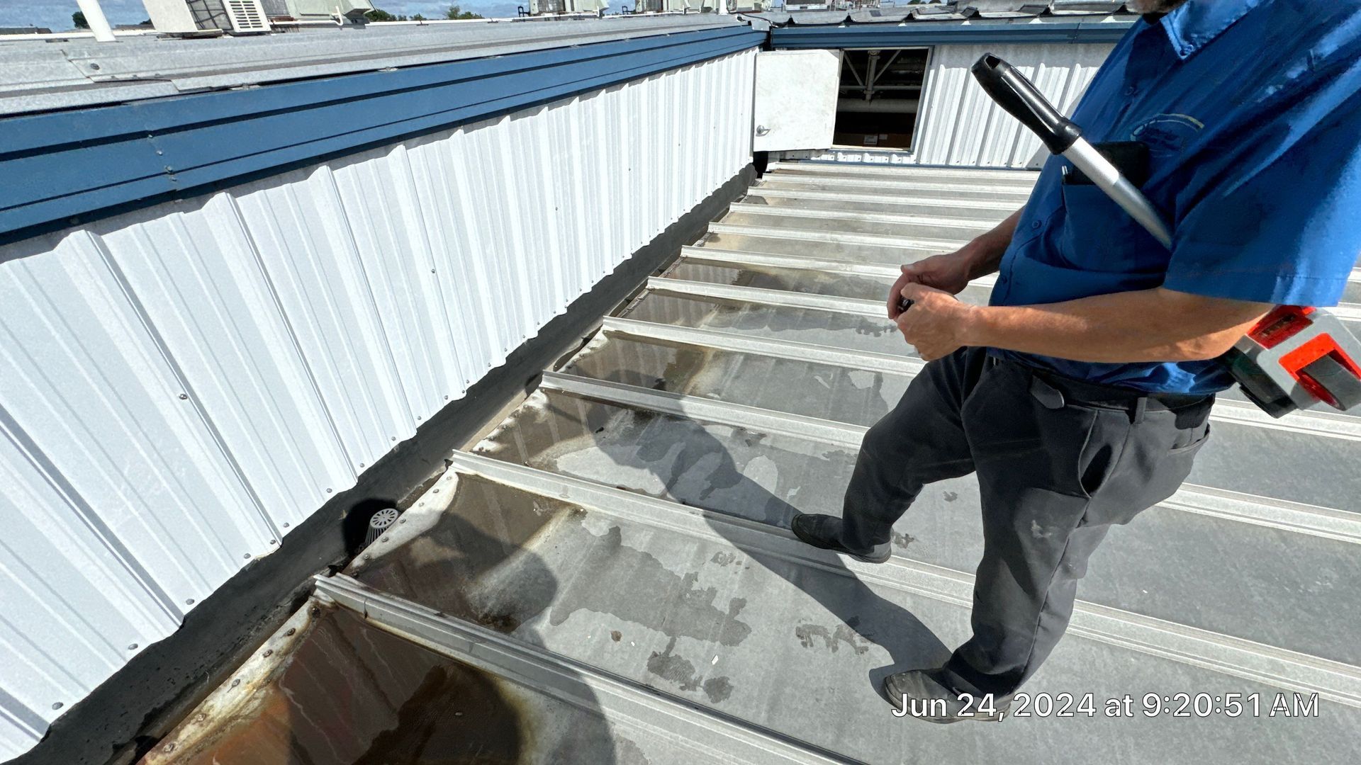 Commercial metal roof on Jalyn Drive showing standing water near wall flashing and roof drains during a leak inspection.