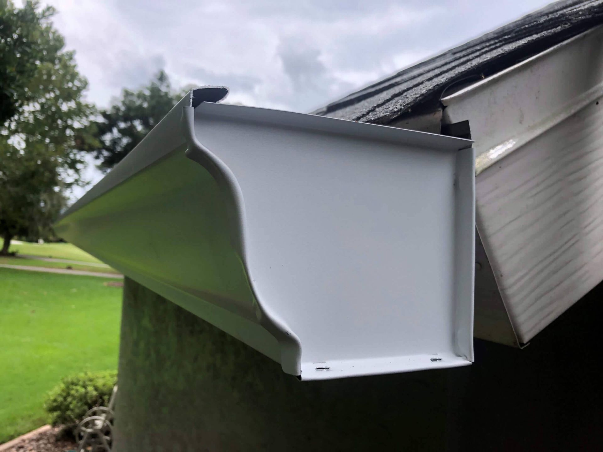 White gutter attached to a dark roof, viewed from below on a cloudy day.