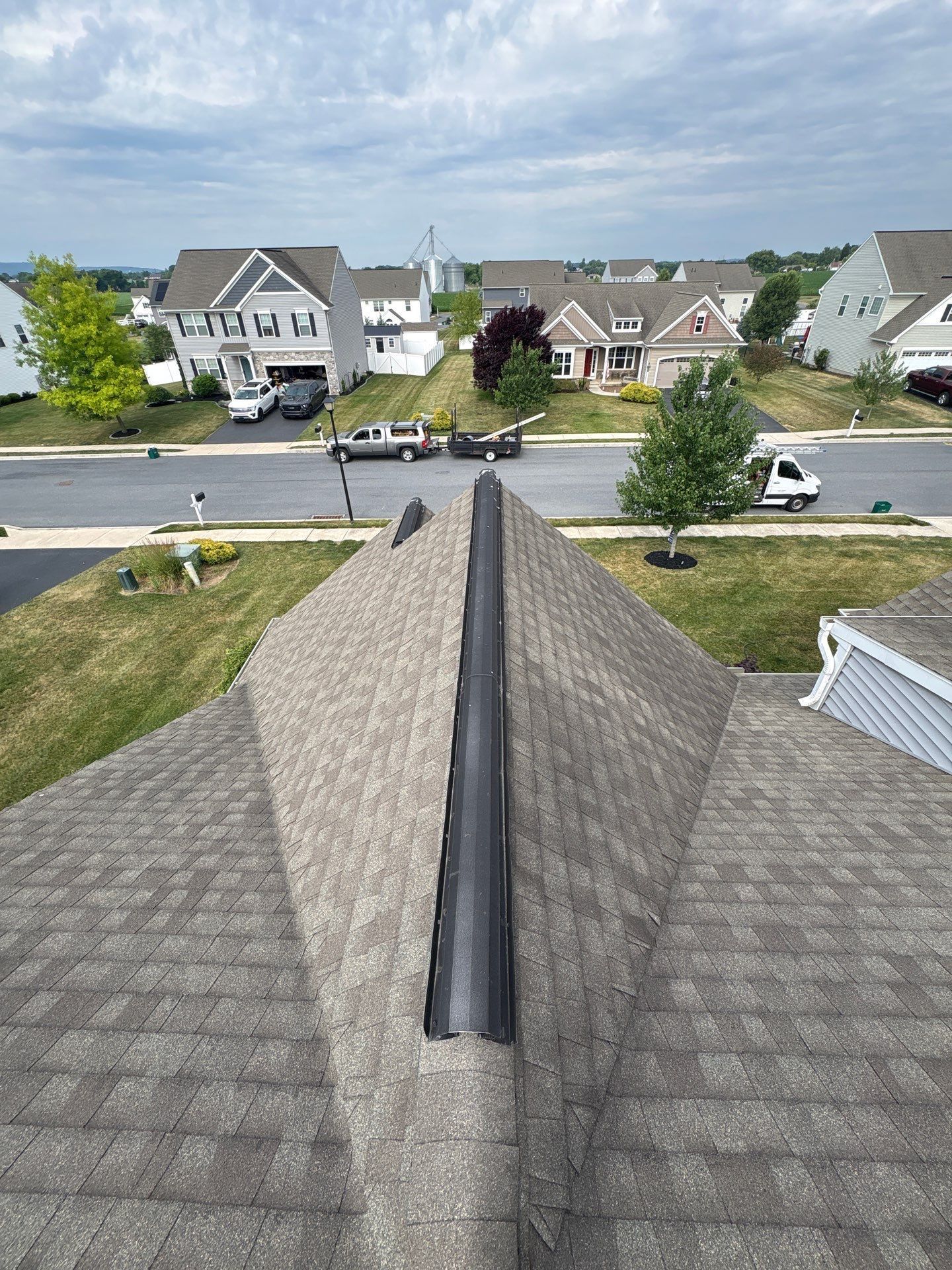 Rooftop ridge with dark shingles overlooking a suburban neighborhood on a sunny day