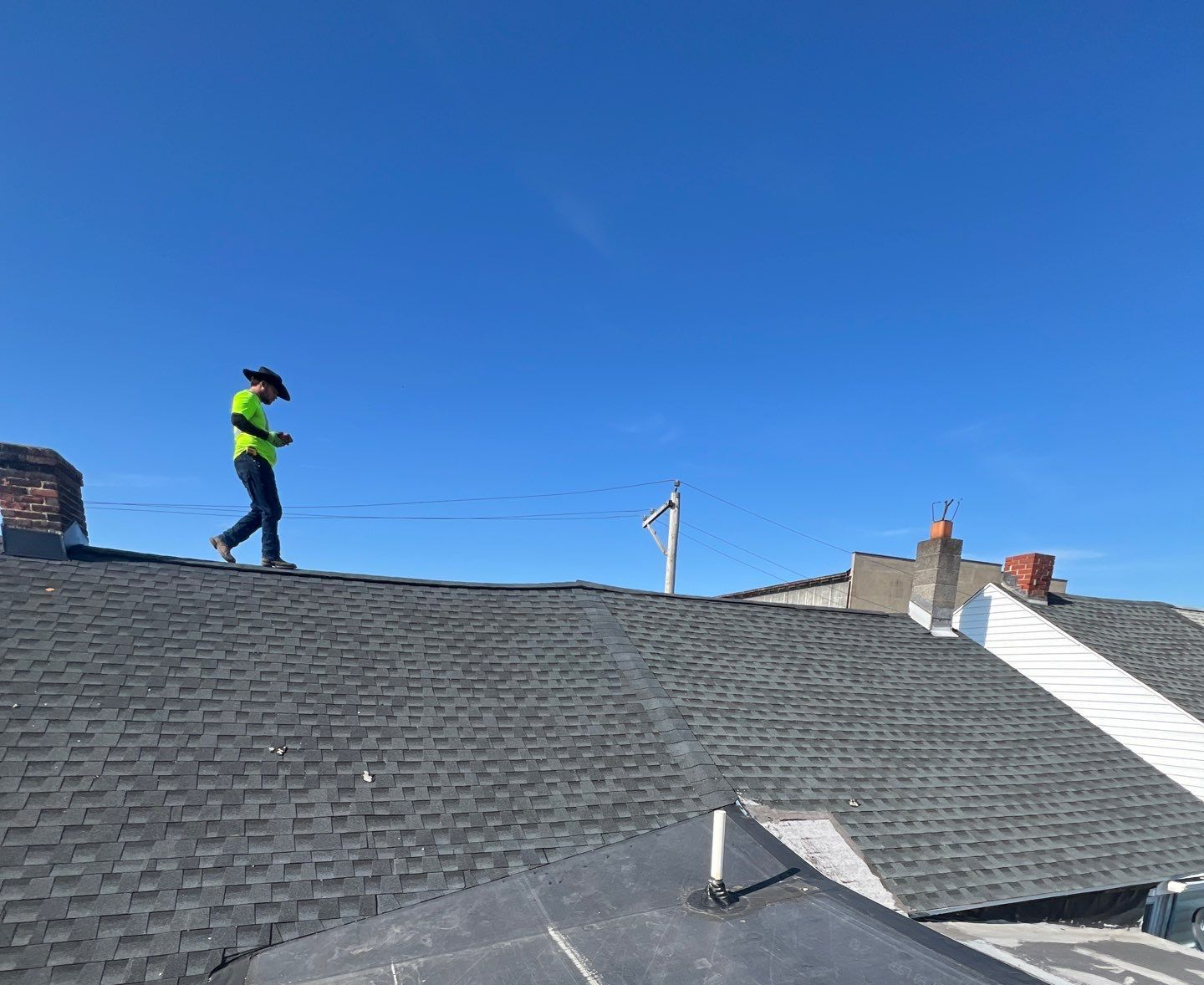 Worker in a safety vest standing on a rooftop under a clear blue sky.