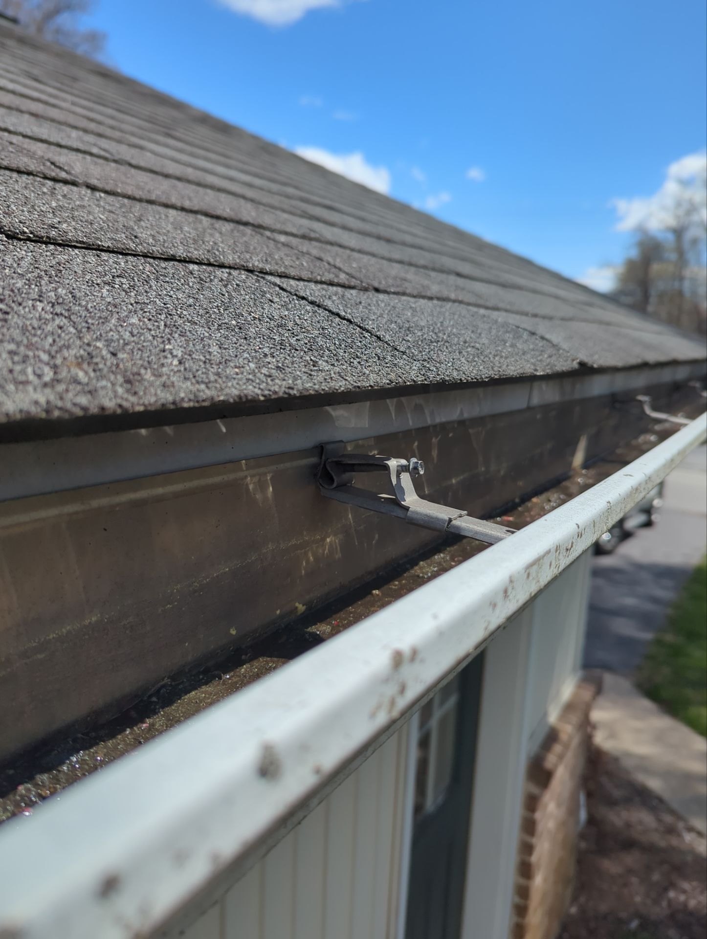 Close-up of an aging residential gutter with a loose hidden hanger, debris buildup, and asphalt shingle roof edge on May Post Office Road in Quarryville, PA.