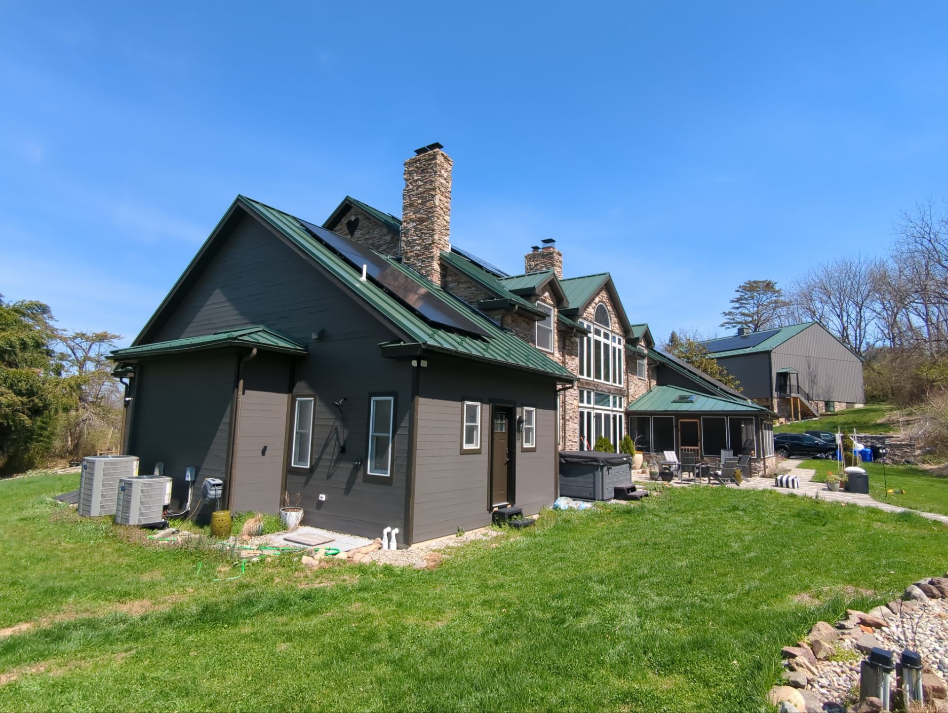 Green house with chimney and porch in a sunny yard, with a stone wall and trees in the background